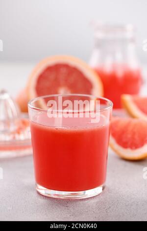 Un bicchiere di succo di pompelmo appena fatto e fette di frutta fresca su uno sfondo di cemento chiaro. H Foto Stock