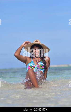 Donna ispanica che si siede su una spiaggia con un bel bikini E cappello di paglia guardare camera.in Los Roques Venezuela Foto Stock