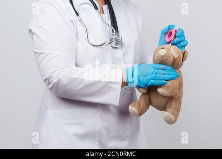 medico femminile in un cappotto bianco e guanti in lattice blu contiene un orsacchiotto marrone Foto Stock