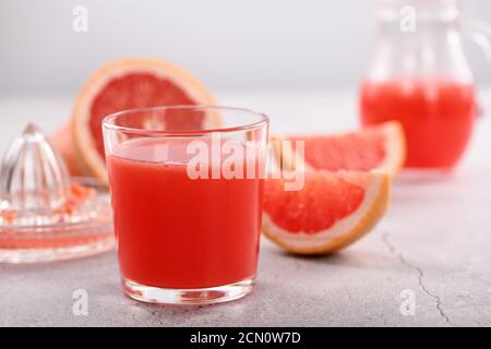 Un bicchiere di succo di pompelmo appena fatto e fette di frutta fresca su uno sfondo di cemento chiaro. H Foto Stock