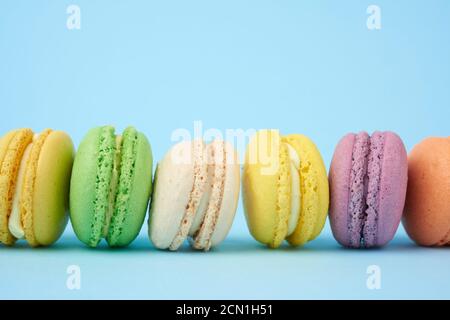 torte di macaron rotonde e multicolore su sfondo azzurro, il dessert si trova in fila Foto Stock