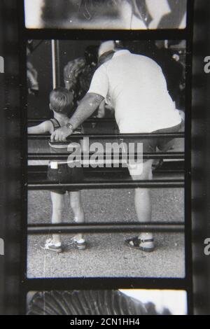 Fine anni '70 vintage fotografia in bianco e nero di un papà aiutare il suo bambino a giocare un gioco di carnevale. Foto Stock