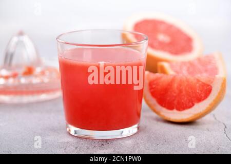 Un bicchiere di succo di pompelmo appena fatto e fette di frutta fresca su uno sfondo di cemento chiaro. H Foto Stock