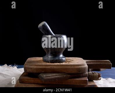 mortaio di pietra nera con pestello per macinare spezie ed erbe su una tavola di legno marrone Foto Stock