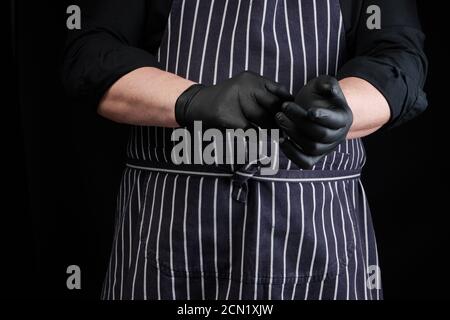 chef uomo in uniforme nera e grembiule a righe abiti in lattice guanti Foto Stock