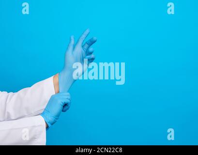 donna medico in un cappotto bianco le mette sulle mani guanti medici sterili in lattice blu sulle mani Foto Stock