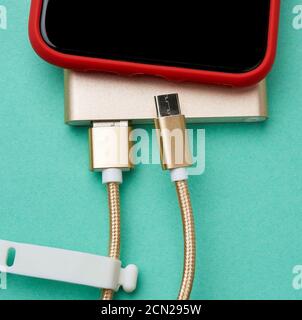 lo smartphone rosso con schermo nero vuoto è collegato tramite cavo a un power bank, sfondo verde Foto Stock