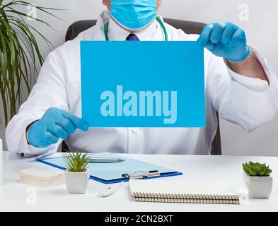 medico in un cappotto medico bianco è seduto ad un tavolo in una sedia di pelle marrone e tenendo un vuoto bl Foto Stock