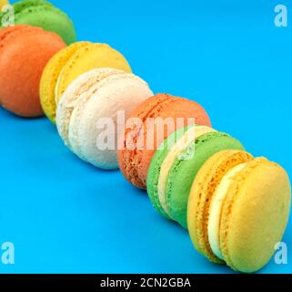 i macaron rotondi e multicolore al forno con panna si trovano in una linea su sfondo blu Foto Stock