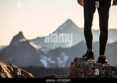 Vista delle gambe e delle scarpe dei corridori arroccati su una cima di montagna. Foto Stock