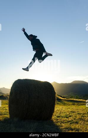 Uomo che salta sopra la balla di fieno alla luce del sole Foto Stock