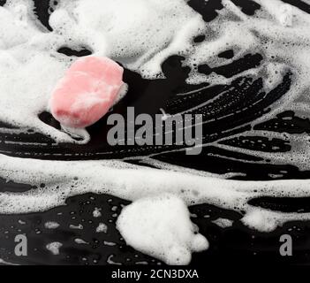 schiuma di sapone bianca e sapone rosa su sfondo nero, vista dall'alto Foto Stock