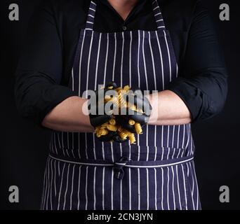 cuoco maschile in un grembiule a strisce e guanti in lattice nero tenere la pasta cruda di fusili Foto Stock