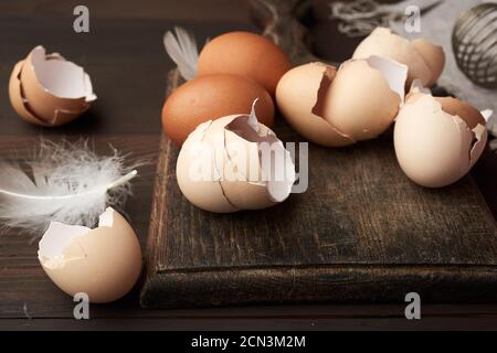 uova di pollo crude, conchiglie, tagliere e frusta a mano per proteine su un tavolo di legno Foto Stock