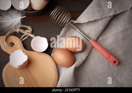 uova di pollo crude, conchiglie, tagliere e frusta a mano Foto Stock