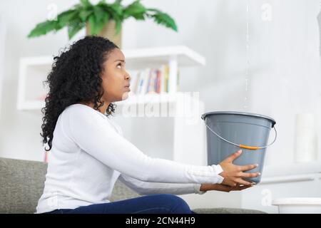 Donna che mantiene la benna mentre le goccioline di acqua perdite dal soffitto Foto Stock