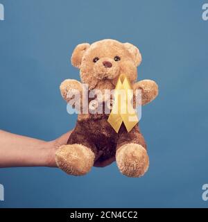 mano femminile tenere un piccolo orsacchiotto con un giallo nastro piegato in un loop Foto Stock