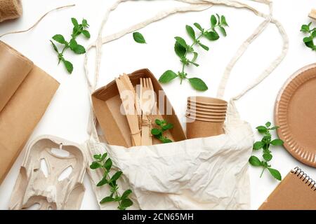 borsa in tessuto e stoviglie monouso di carta da artigianato marrone, foglie di menta verde su sfondo bianco Foto Stock