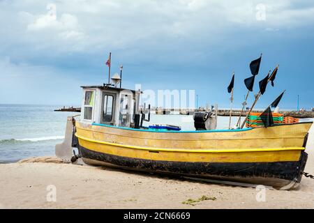 Arrugginita barca da pesca sulla spiaggia sabbiosa con molo e blu mare sullo sfondo Foto Stock