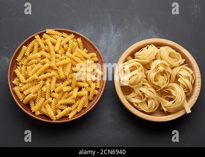 fusilli crudi e fettuccine in piatti di legno su a. tavolo nero Foto Stock