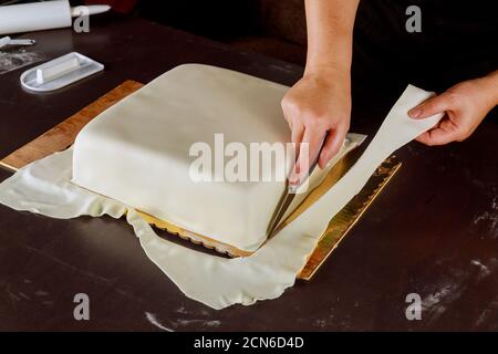 Confectioner che taglia il fondante bianco su cake.Technique quadrato di fare la torta di nozze. Foto Stock