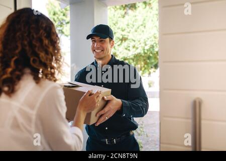 Sorridente uomo di consegna che consegna una scatola a una femmina a casa. Corriere lavoratore che consegna un pacco a donna. Foto Stock