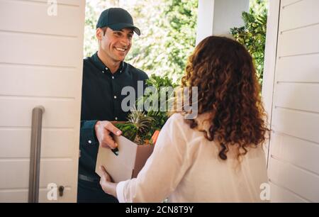 L'uomo di consegna consegna passa sopra la scatola degli alimentari alla porta della casa. Addetto alla consegna che consegna una scatola di frutta e verdura a una donna. Foto Stock