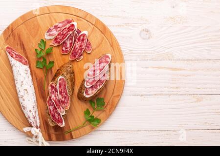 Salame e pane su fondo di legno bianco. Vista dall'alto. Spazio di copia Foto Stock