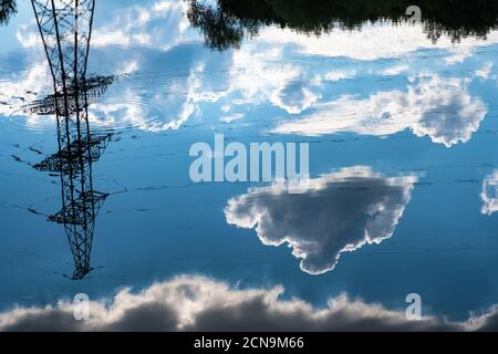 Riflesso di una linea di alimentazione e oscure nubi di cumulo in acqua in un giorno d'estate. Foto Stock