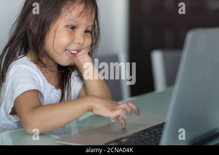 Carino bambina asiatica felice di utilizzare un computer portatile a casa a casa a casa a scuola. Foto Stock