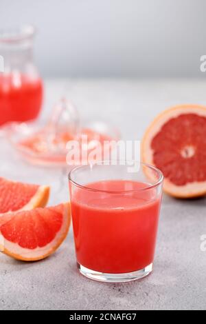 Un bicchiere di succo di pompelmo appena fatto e fette di frutta fresca su uno sfondo di cemento chiaro. H Foto Stock