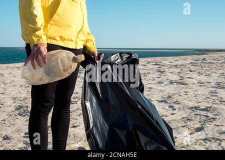 Donna che raccoglie rifiuti e plastica che pulisce la spiaggia con un sacco per rifiuti. Attivista volontario ambientale contro il cambiamento climatico e l'inquinamento o Foto Stock