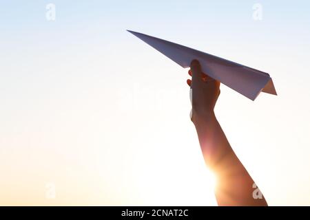 La mano tiene l'aeroplano di carta e lancia sullo sfondo del sole luminoso Foto Stock