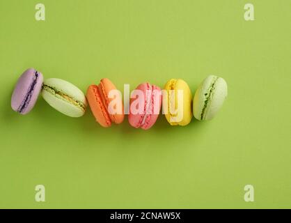 i biscotti di macaron multicolore cotti al forno si trovano in una fila su un sfondo verde Foto Stock