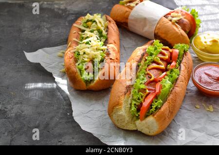 Hot dog con vari riempimenti. Sfondo scuro. Cibo sfondo con spazio di copia. Hot dog con senape e ketchup, lattuga, formaggio e pomodori Foto Stock