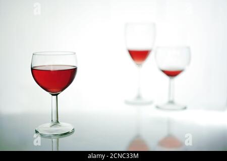 Bicchiere con vino rosso in primo piano, due più sfocati dietro, sfondo blu grigio chiaro con spazio per la copia, messa a fuoco selezionata, reparto stretto Foto Stock