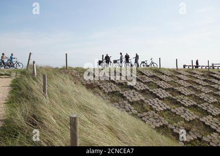 Pista ciclabile con ciclisti sulla diga olandese (Hondsbosche Zeewering) vicino Petten. Dune artificiali di fronte alla diga. Settembre, Paesi Bassi. Foto Stock