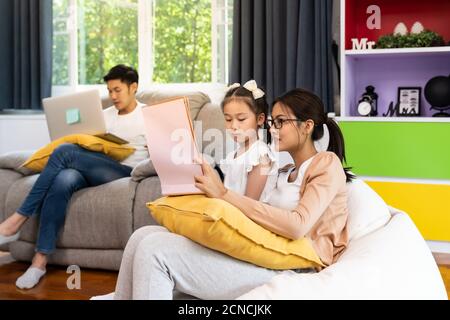 Mamma che legge la storia di daugther mentre il papà lavora da casa Foto Stock