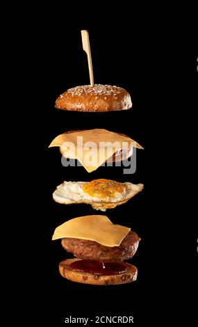 cheeseburger volanti ingredienti: cotoletta di carne, panino di semi di sesamo, formaggio, uova fritte e ketchup di pomodoro Foto Stock