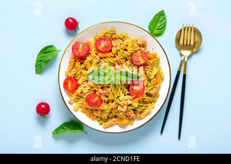 Fusilli - classica pasta italiana di grano duro con carne di pollo, pomodori ciliegia, basilico in salsa di pomodoro in ciotola bianca su tavola di legno blu Foto Stock