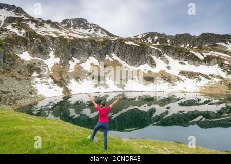 Donna allegra con braccia distese sulle rive dei laghi di Porcile, della Valle del Tartano, della Valtellina, della Lombardia, dell'Italia, dell'Europa Foto Stock