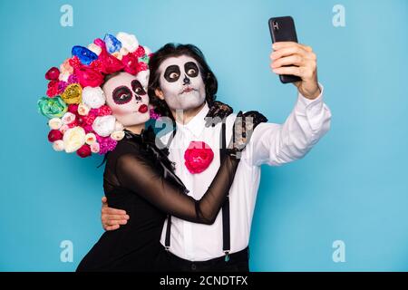 Foto di simpatico zombie divertente coppia uomo donna abbraccio ragazza hold telefono fare selfie tradurre festival indossare abito nero morte fascia costume roses Foto Stock