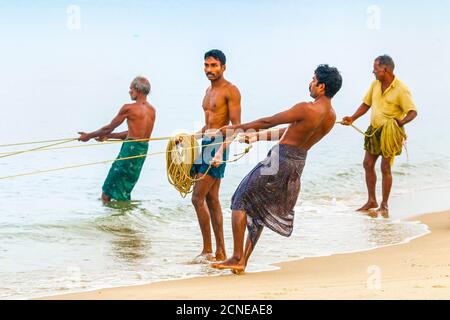 I pescatori che tirano la grande rete di insieme a riva a occupato, popolare spiaggia di Marari, Mararikulam, Alappuzha (Alleppey), Kerala, India, Asia Foto Stock