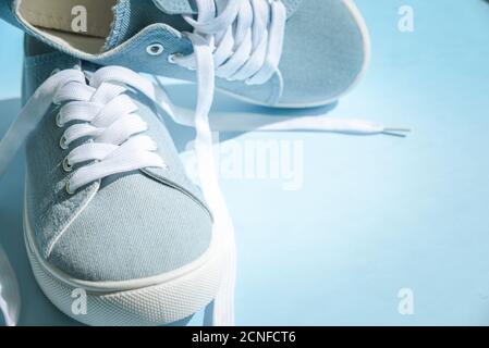 Sneaker blu con lacci bianchi su sfondo azzurro. Elegante concetto informale alla moda. Foto Stock