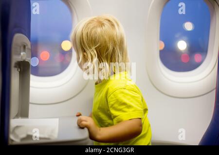 Bambino, bambino che salta in aereo, seduto e in attesa di partenza, giocando con i giocattoli, sorridendo felice Foto Stock