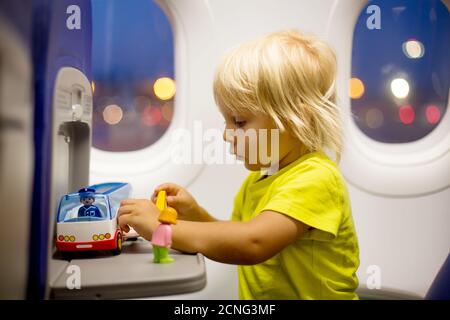 Bambino, bambino che salta in aereo, seduto e in attesa di partenza, giocando con i giocattoli, sorridendo felice Foto Stock