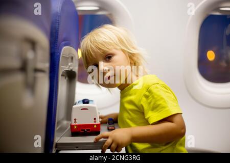 Bambino, bambino che salta in aereo, seduto e in attesa di partenza, giocando con i giocattoli, sorridendo felice Foto Stock