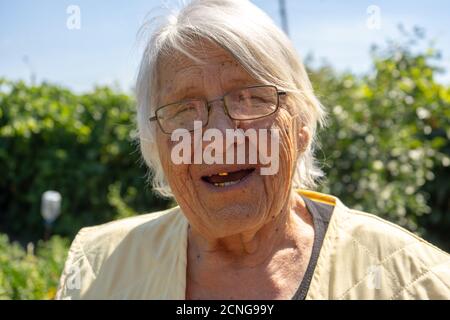 vecchia signora bella faccia e capelli grigi, donna anziana nel suo giardino, nonna sorridente da vicino Foto Stock