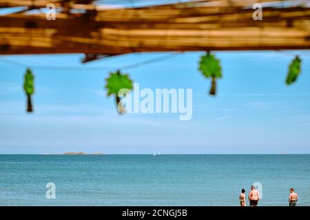 Palm tree a forma di stringa di festa luci su un rustico bar sulla spiaggia cafe con il blu del mare e del cielo la spiaggia con i bagnanti - quirky tropical beach vacanze estate Foto Stock