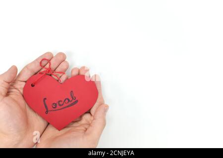 Le mani di giovane maschio che tengono un'etichetta rossa di forma del cuore con la parola scritta a mano locale. Supporto, amore, acquisto e campagna per il concetto di piccola impresa locale. Disposizione piatta Foto Stock